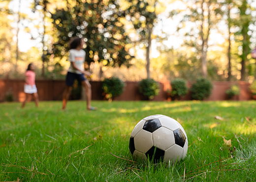 Soccer ball laying on a lawn with children playing in the background.