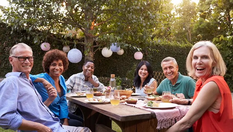 A picture of of a group of people sitting at an outdoor table enjoying a picnic.