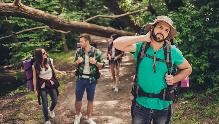 A man on a hike with friends swatting at a mosquito on their neck.