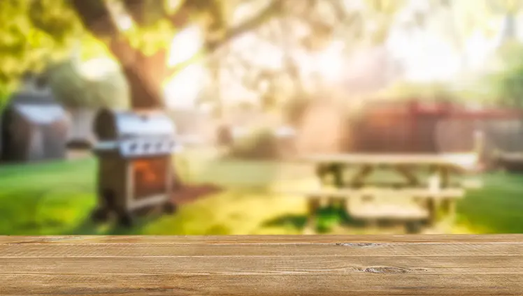 A closeup of a picnic table in a backyard with a gas grill and another picnic table in the background.