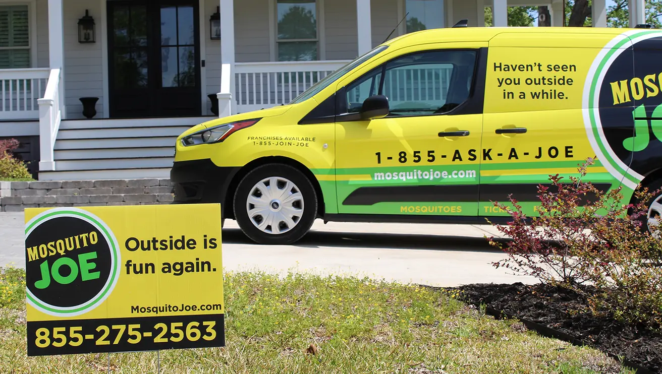 Mosquito Joe van sitting in the driveway of a customer with a Mosquito Joe sign in their yard.