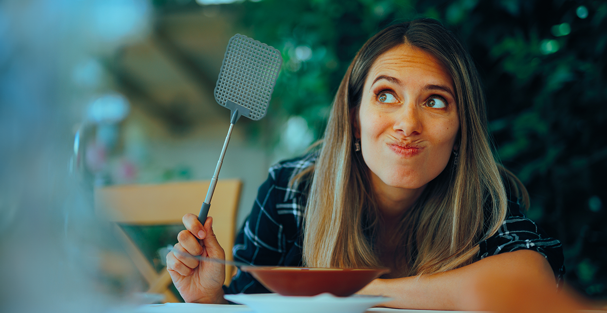 Woman holding a fly swatter while focusing on catching a fly.