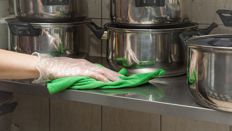 A hand wearing a latex glove cleaning a surface with a cloth.