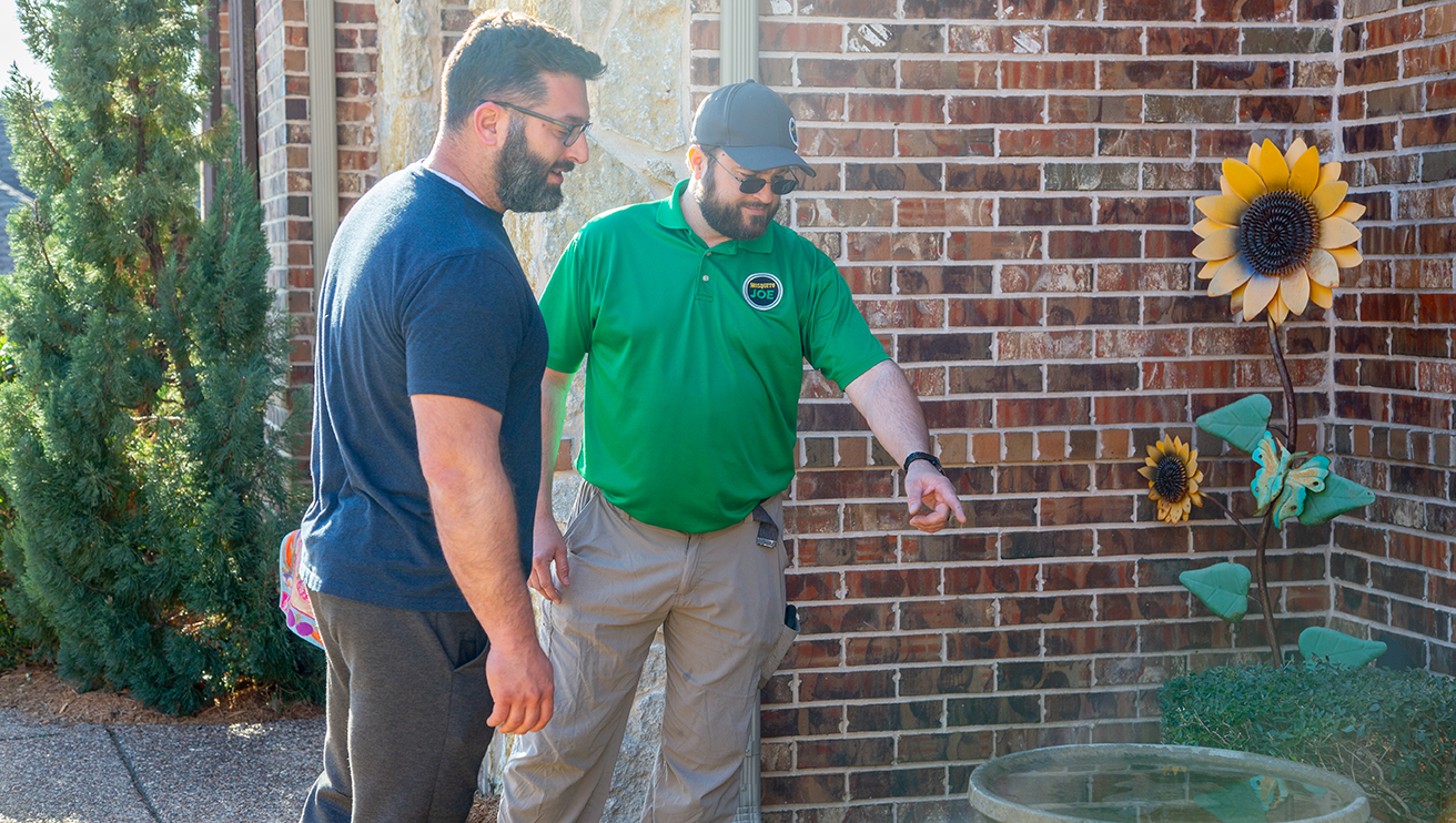 A Mosquito Joe employee showing a customer water build-up near a wall.