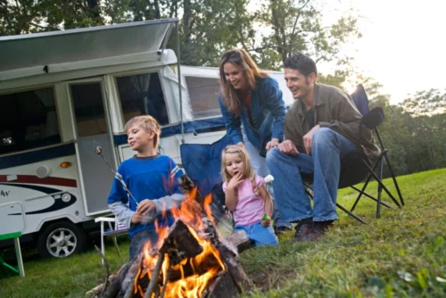 Family sitting around campfire with smores outside of RV