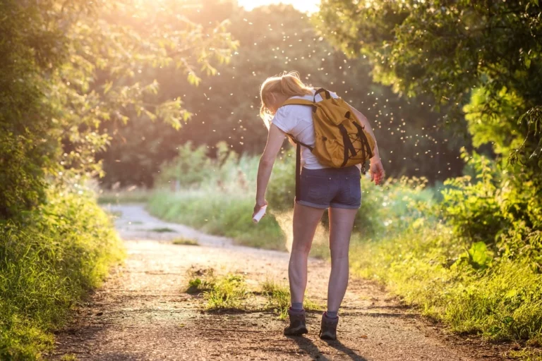 Woman hiker spraying bug spray while walking down trail