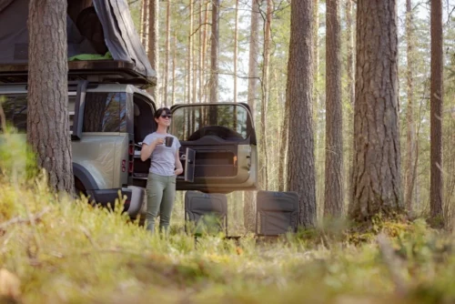 Woman standing drinking coffee outside of RV while camping in the woods